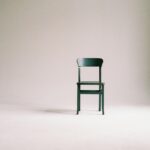 A single black chair in a minimalistic studio setting with a neutral backdrop.